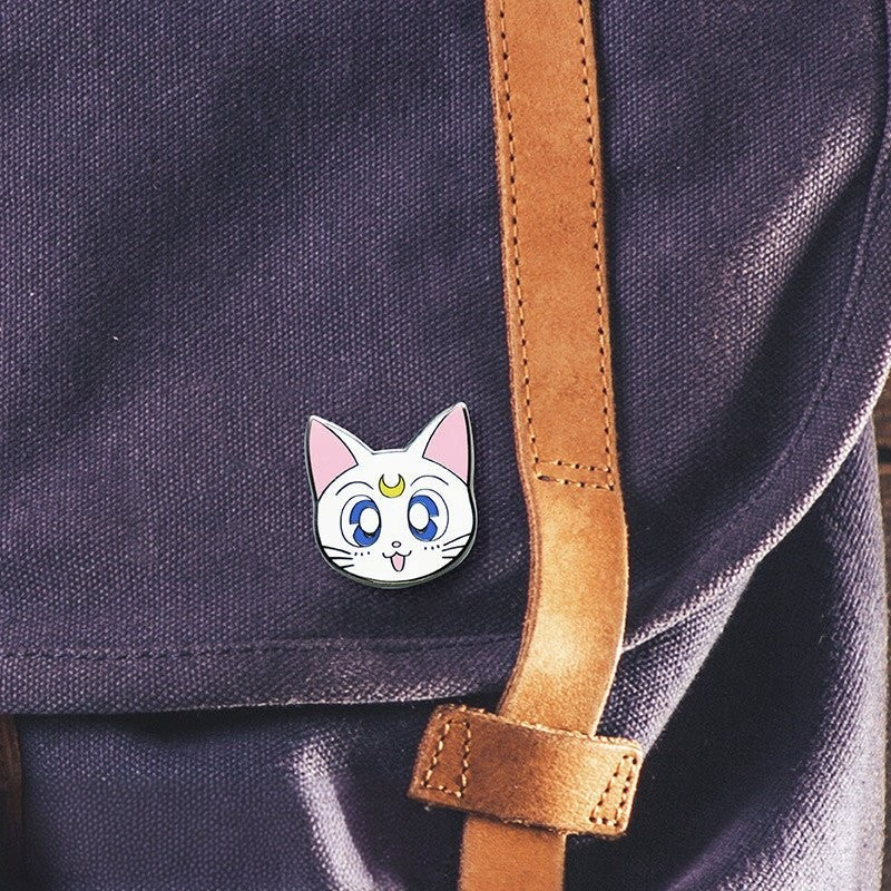Fans Geek Store Sailor Moon Artemis metal pin attached to a purple fabric backpack with a brown leather strap