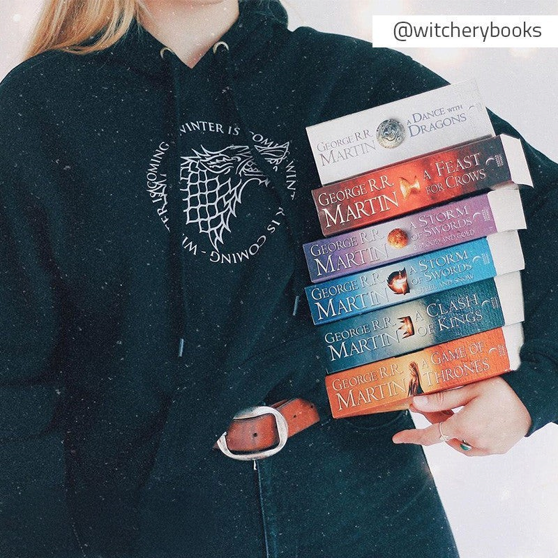 Fans Geek Store black House Stark hoodie with wolf sigil worn by a person holding a stack of Game of Thrones books