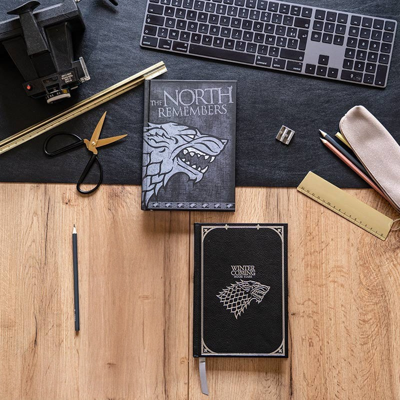 Fans Geek Store Game of Thrones House Stark notebooks with embossed wolf sigils and gold foil on a wooden desk
