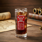 Fans Geek Store One Piece Luffy glass with red Jolly Roger logo filled with cola on a wooden table